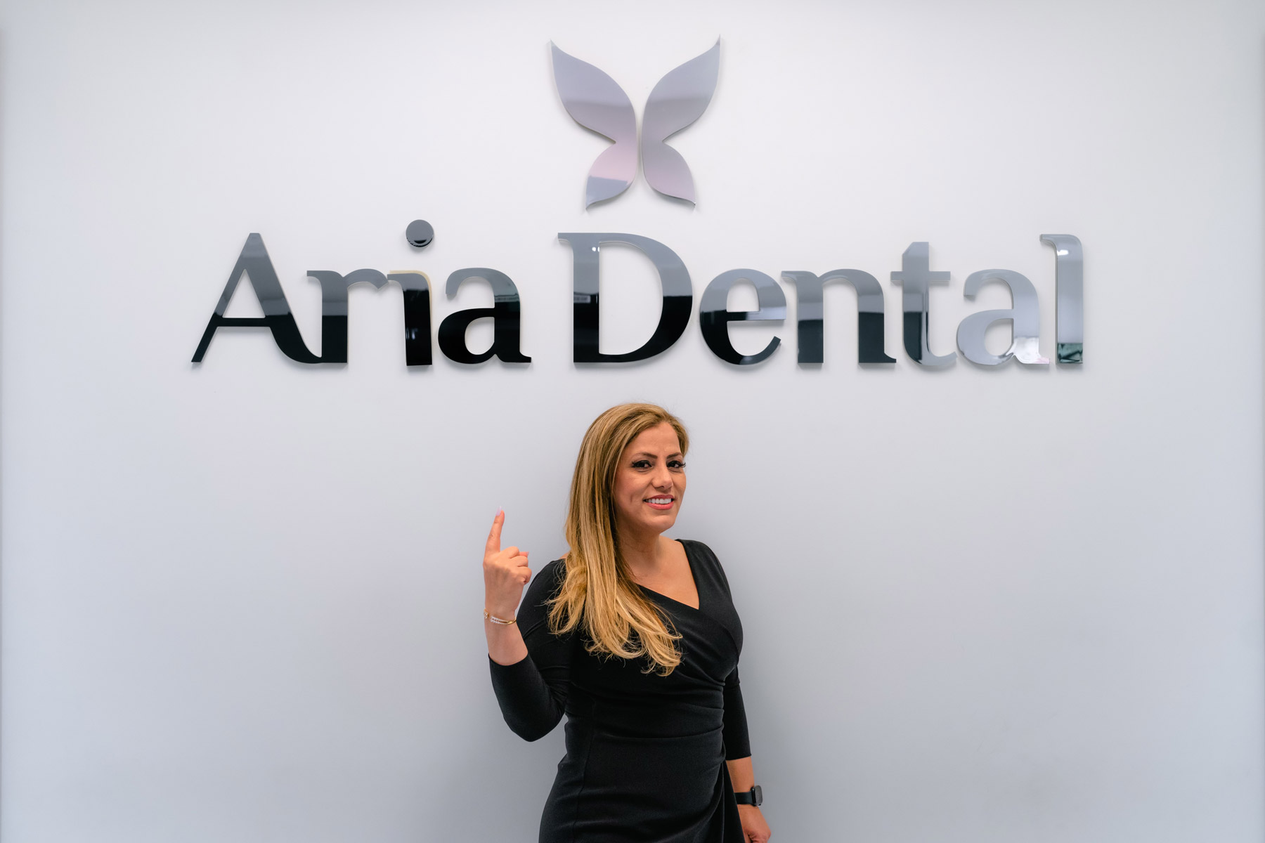 Dr. Maryam Horiyat pointing at Aria Dental Logo