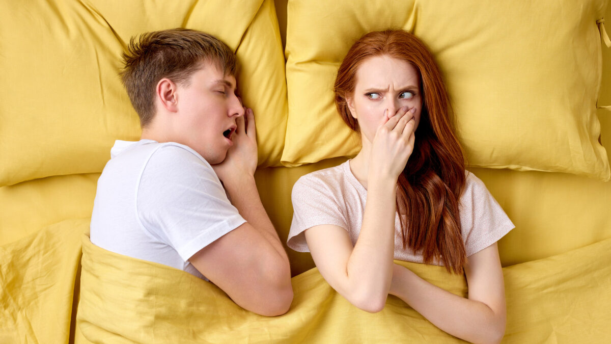 young woman bothered by bad breath of her husband in bed