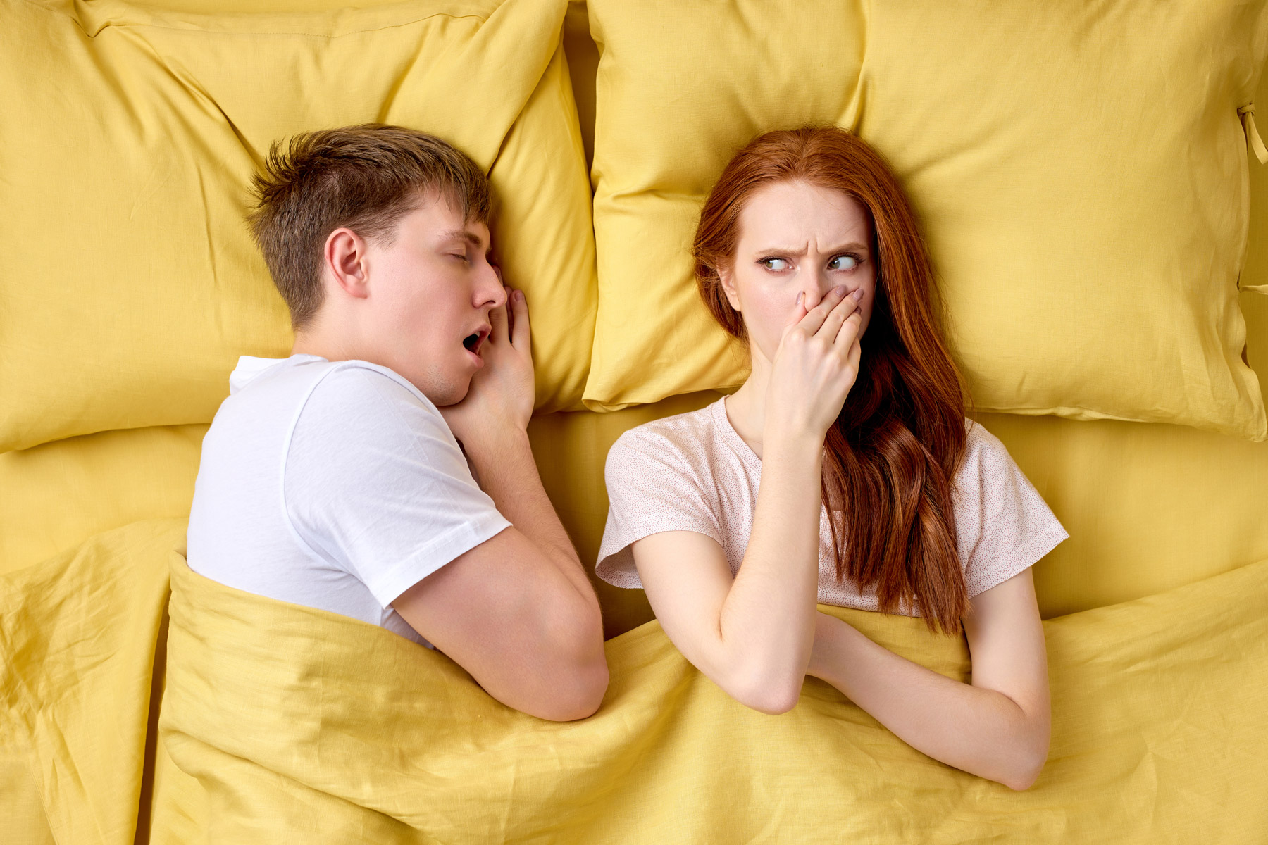 young woman bothered by bad breath of her husband in bed