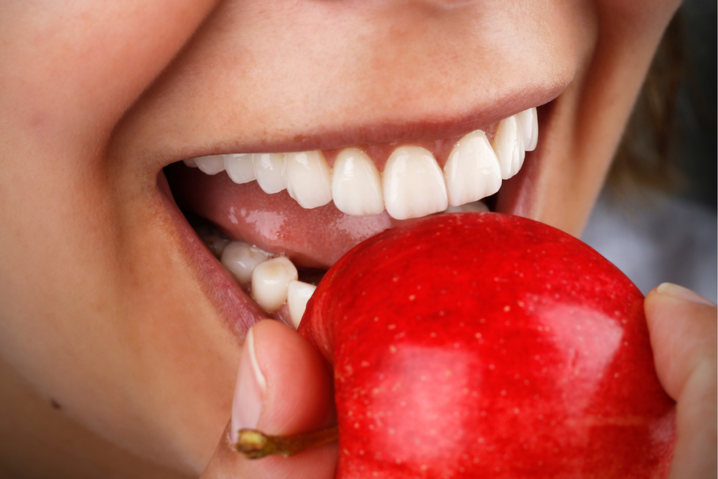 How Long Do Zirconia Crowns Last - Happy woman taking a bite from a red apple with her zirconia crowns